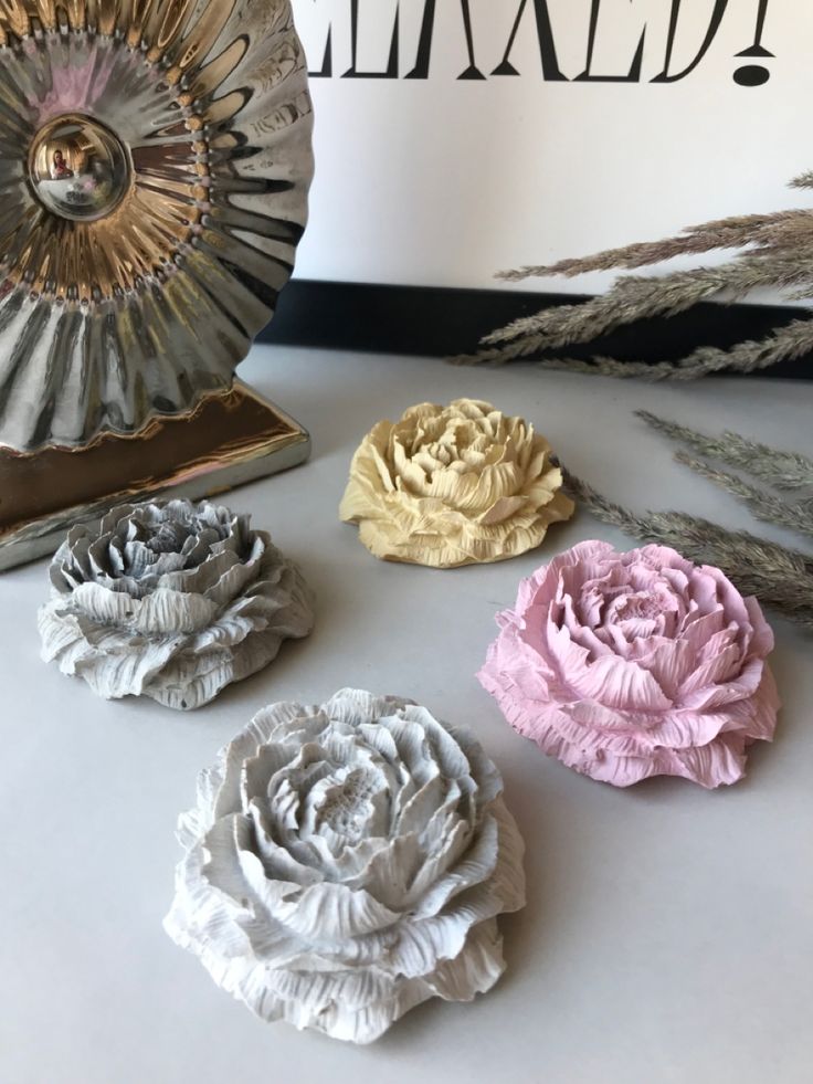 Paeonia Bloom handcrafted ceramic sculptural flowers in four colorways — Pebble Grey, Ivory Dusk, Blush Rose, and Silver Mist — displayed on a white surface with dried botanicals